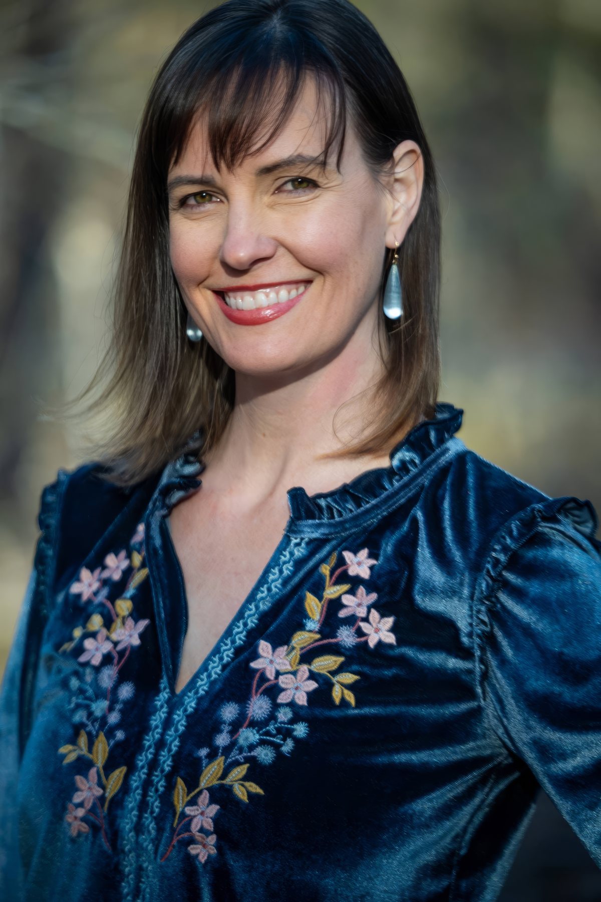 Ashley Oros smiling in a teal embroidered blouse.